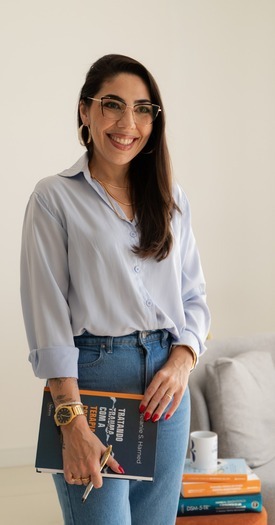 Larissa Bez em pé segurando um livro técnico de terapia cognitivo-comportamental