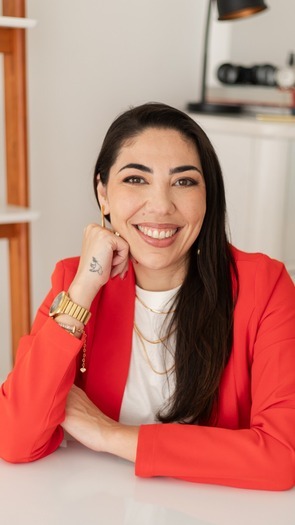 Retrato de Larissa Bez sorrindo, de blazer vermelho